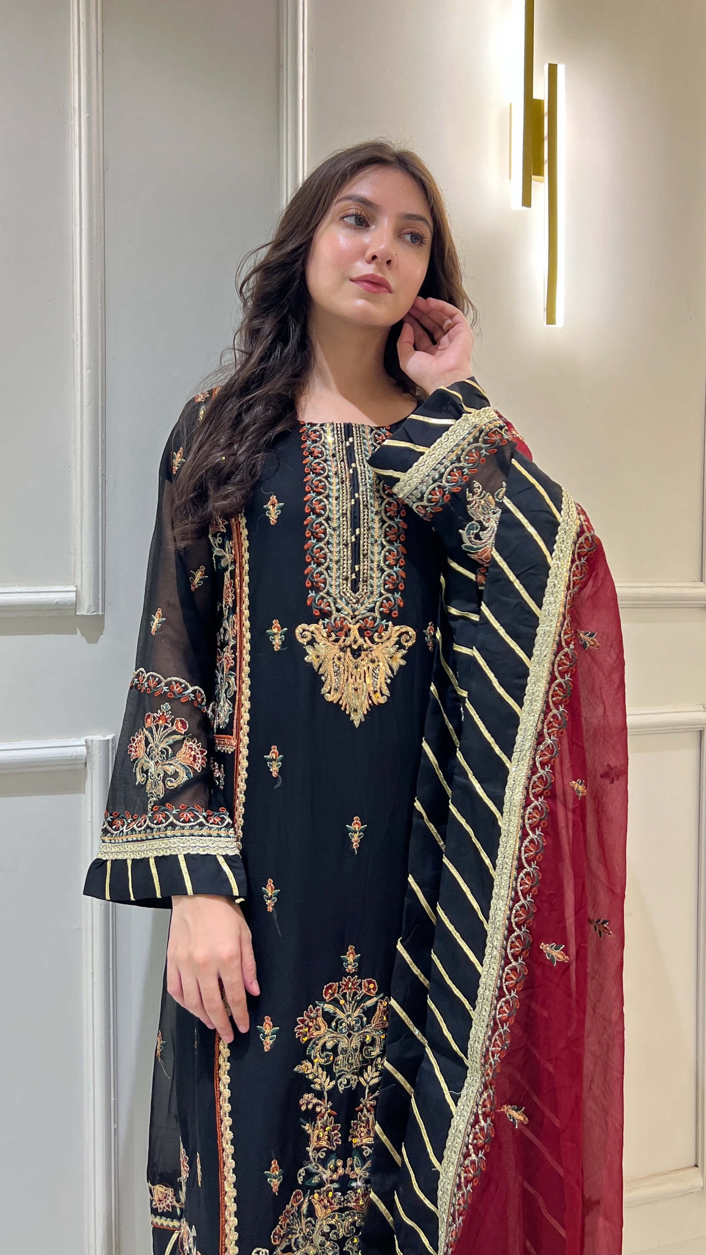 Side profile of woman in embroidered black shalwar kameez with contrast maroon chiffon dupatta
