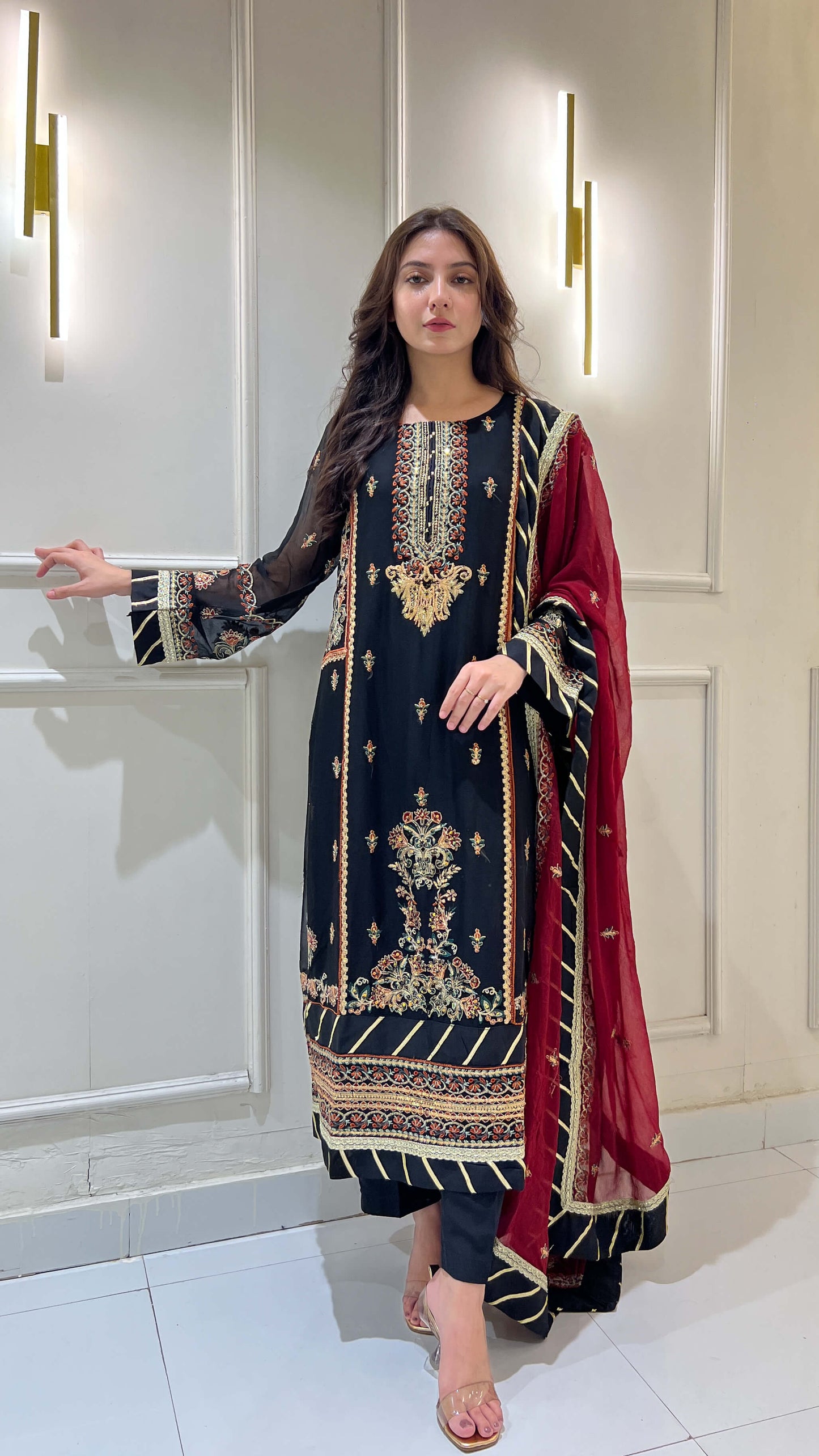 Woman wearing black chiffon embroidered shalwar kameez with maroon dupatta, standing in traditional pose