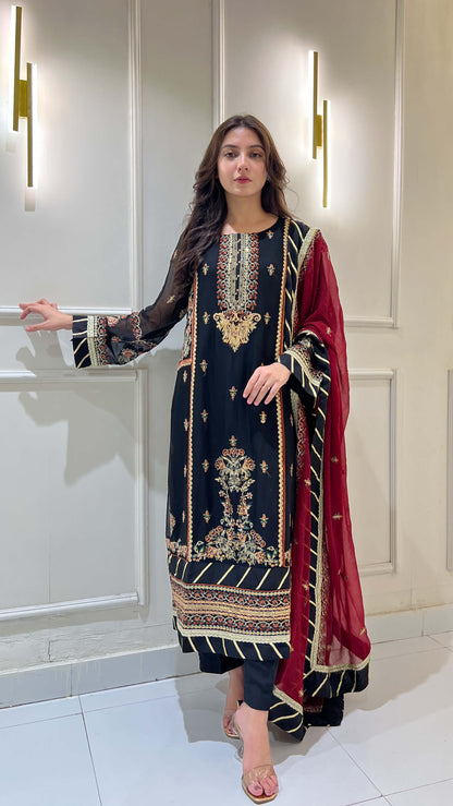 Woman wearing black chiffon embroidered shalwar kameez with maroon dupatta, standing in traditional pose