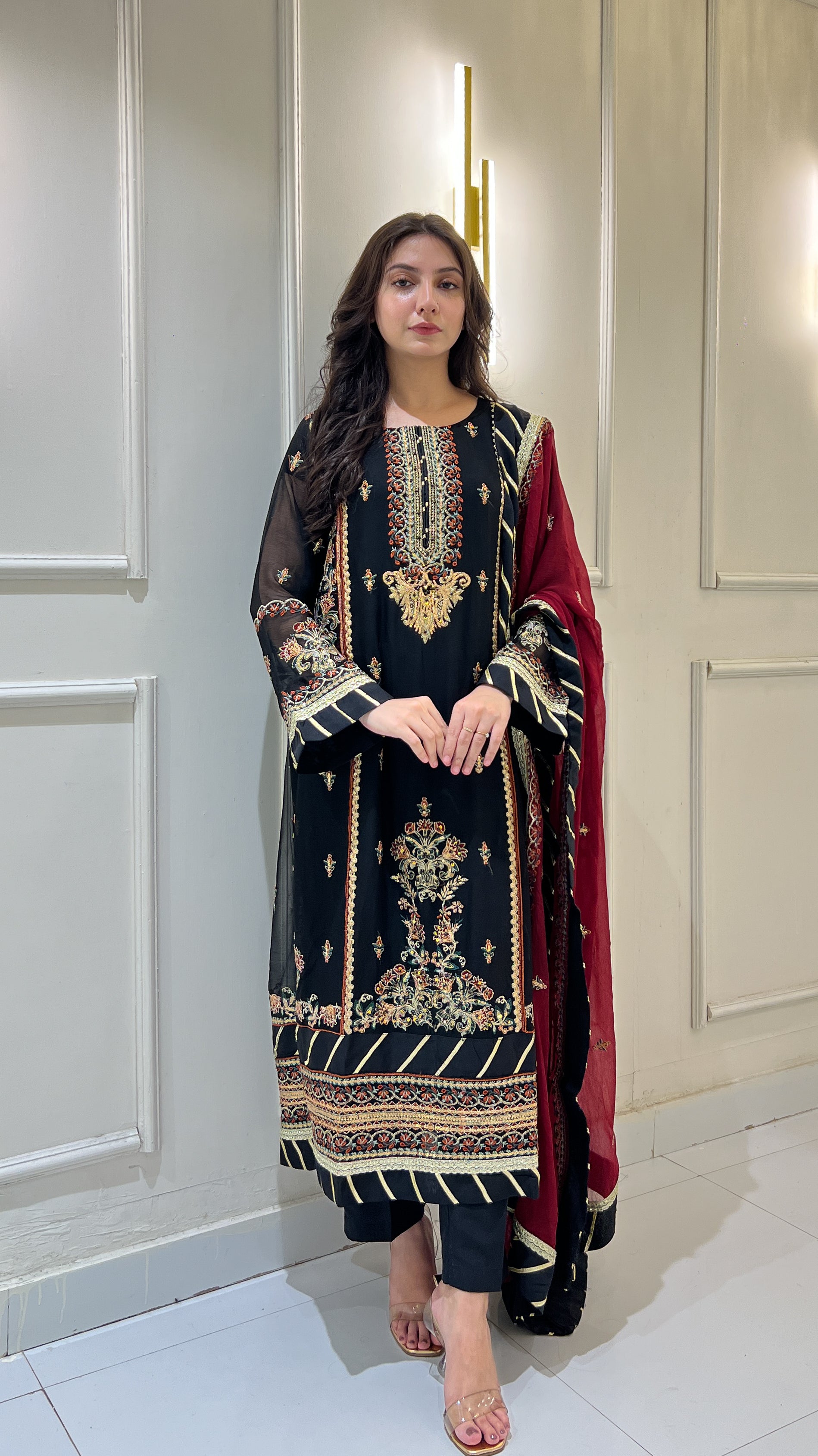 Woman wearing black chiffon embroidered shalwar kameez with maroon dupatta, twirling and showing dress in video
